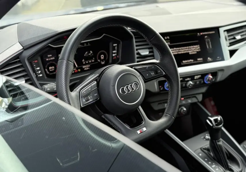 Vue rapprochée du volant sport multifonctions cuir de l'Audi A1 Sportback 30 TFSI 110 S-Tronic Competition, tableau de bord digital visible.