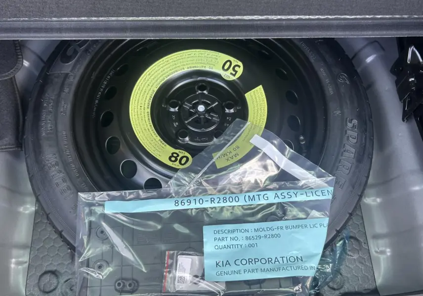 Gros plan sur la roue de secours noire dans le coffre du Kia Sportage 2026, avec un kit de fixation et étiquette visible.