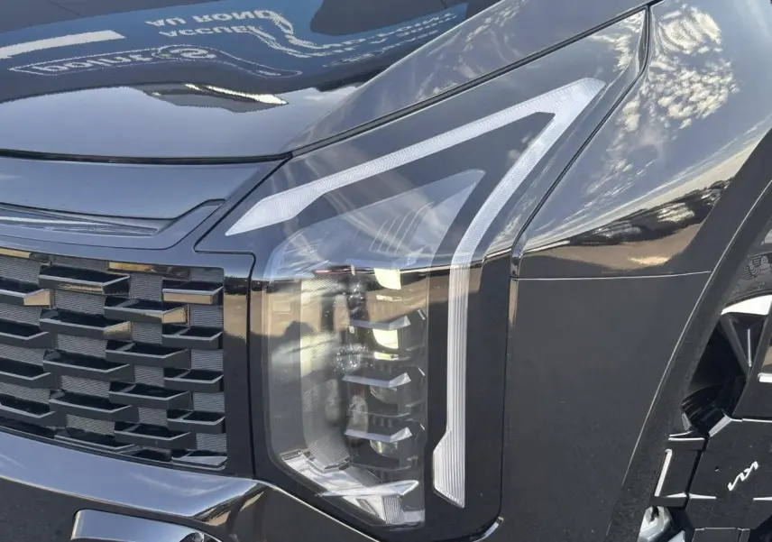 Gros plan sur le phare avant droit noir métallisé du KIA SPORTAGE 2026 avec calandre et jante alliage visibles.