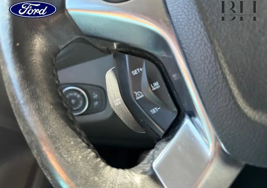 Gros plan sur les commandes de régulateur de vitesse au volant en cuir du Ford Transit Connect gris lunaire.