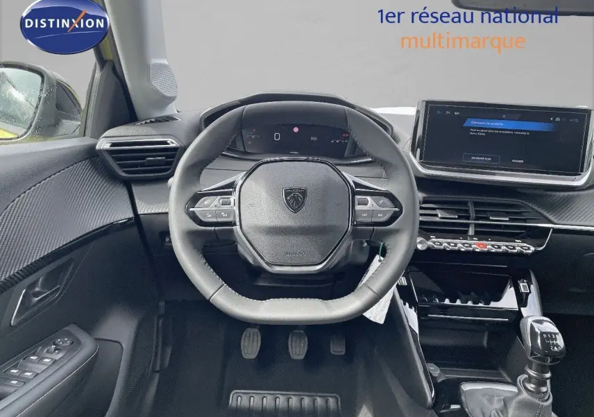 Vue intérieure centrée sur le poste de conduite d'une Peugeot 208 1.2 PureTech avec volant multifonction et boîte manuelle.