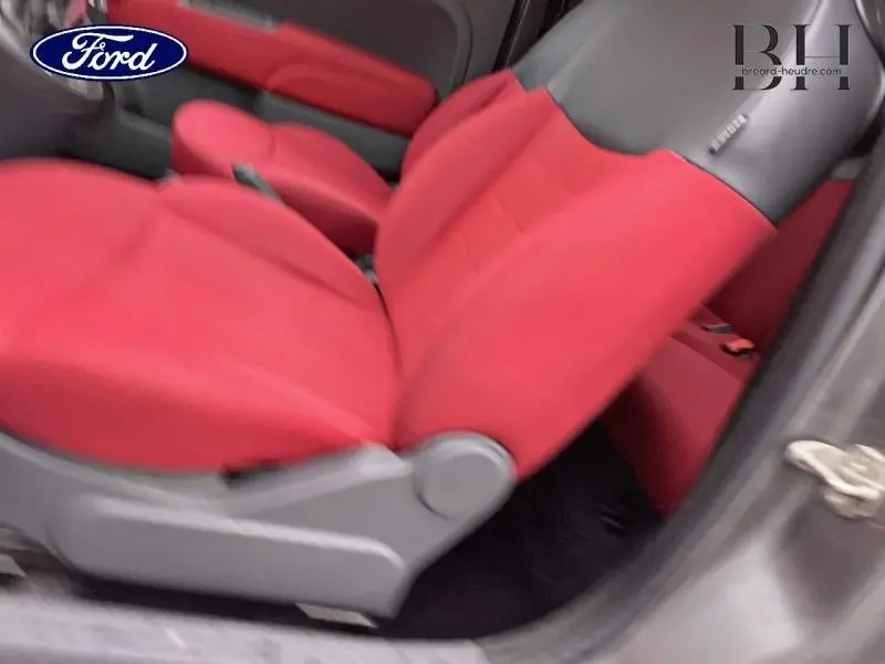 Vue latérale intérieure montrant les sièges avant rouges d'un véhicule, avec une portière ouverte.