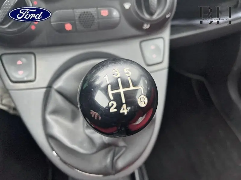 Le levier de vitesses manuel noir en gros plan dans l'habitacle d'une Fiat 500, avec marquages des rapports visibles.