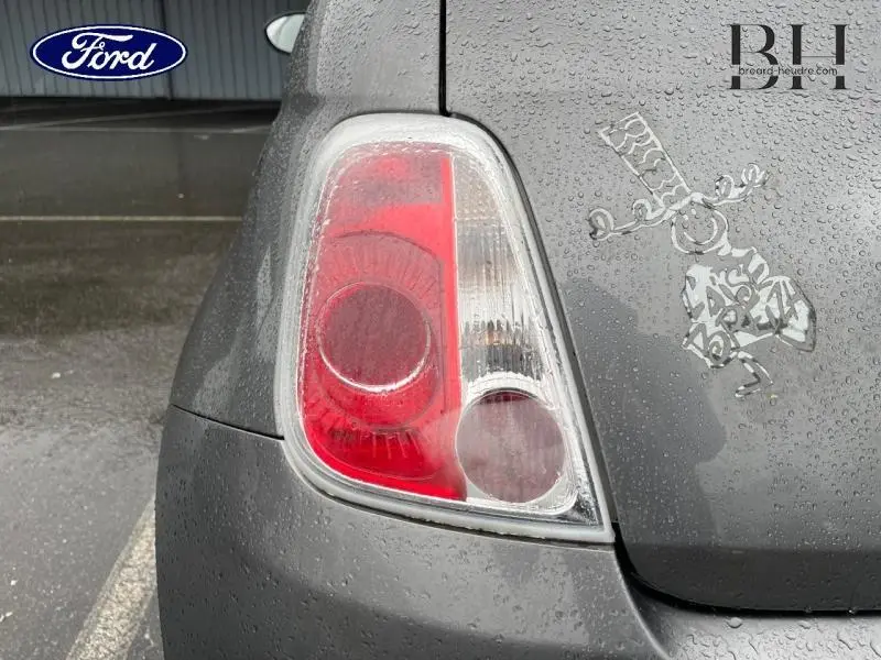 Gros plan sur le feu arrière gauche d'une FIAT 500 marron avec gouttes de pluie et autocollant décoratif sur le coffre.