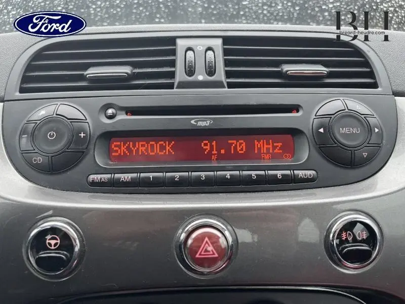 Vue rapprochée de la radio CD MP3 intégrée au tableau de bord gris d'une Fiat 500 marron, affichant la station Skyrock.