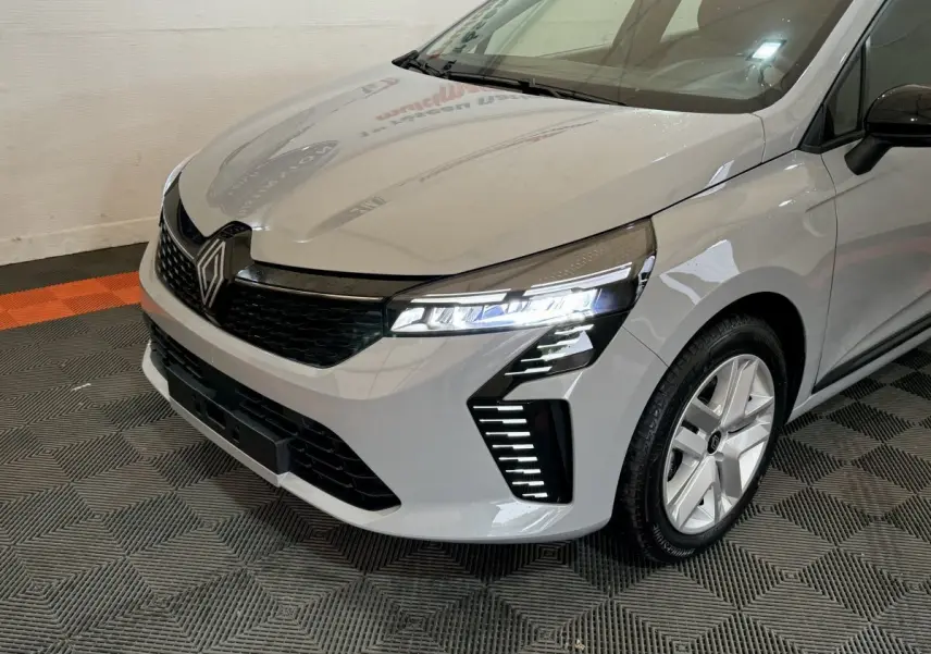 Vue 3/4 avant droit d'une Renault Clio gris clair avec phares LED allumés et calandre noire brillante.