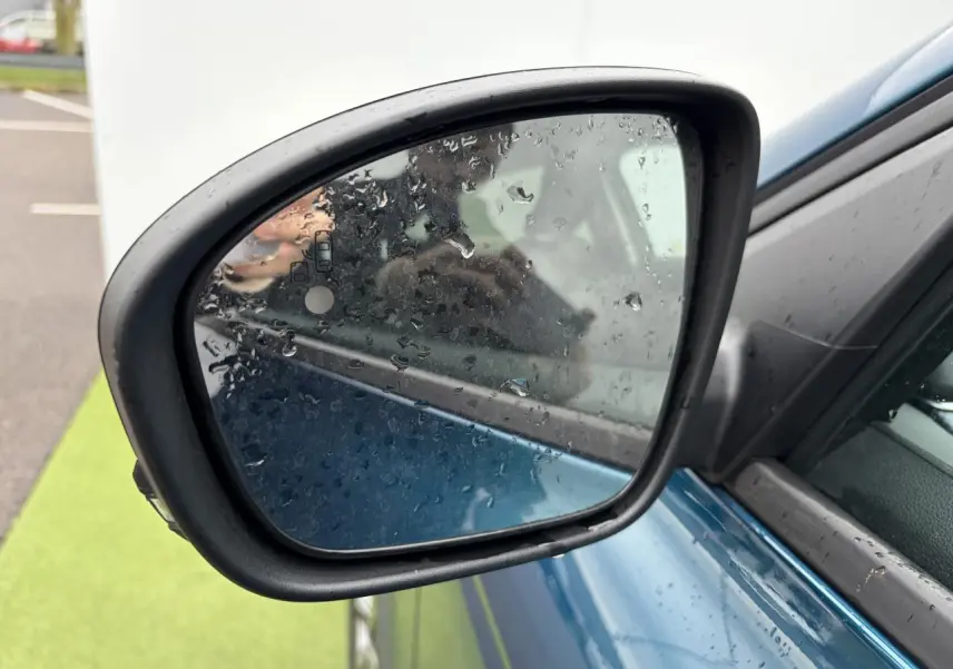Rétroviseur droit d’un Renault Arkana bleu Zanzibar métal avec gouttes de pluie sur le miroir, vue rapprochée.