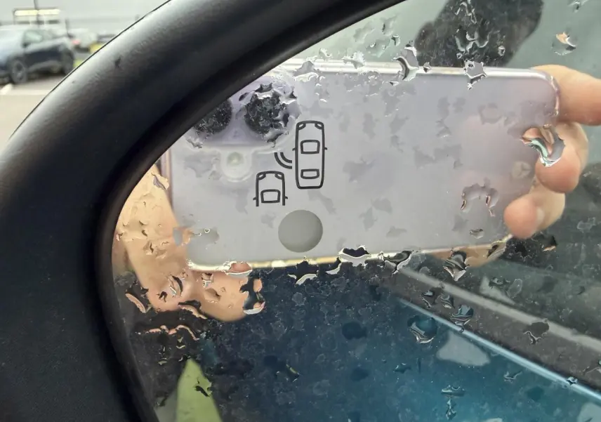 Rétroviseur côté gauche de Renault Arkana bleu Zanzibar, avec icône d'alerte d'angle mort visible sous pluie.