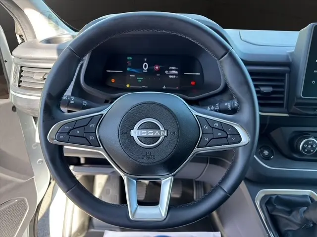 Vue rapprochée du volant cuir noir du Nissan Primastar gris clair, avec tableau de bord numérique et commandes multifonctions.