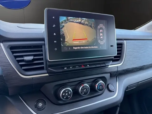 Vue rapprochée de l’écran tactile central affichant la caméra de recul du Nissan Primastar gris clair, avec commandes climatisation et bouton démarrage.