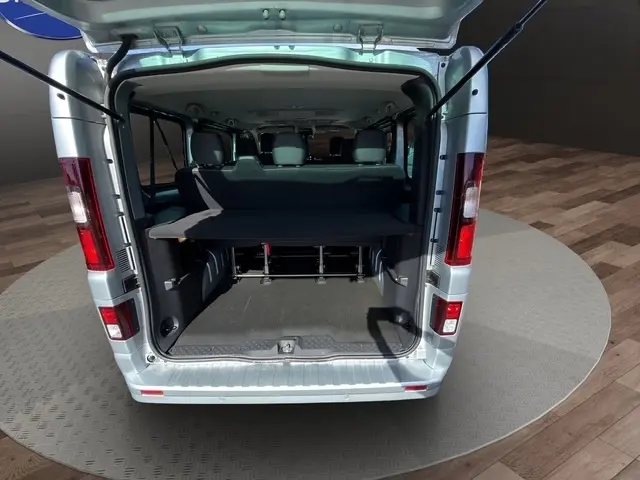 Vue arrière ouverte du Nissan Primastar gris clair 2025, montrant l'espace de chargement et les sièges arrière.