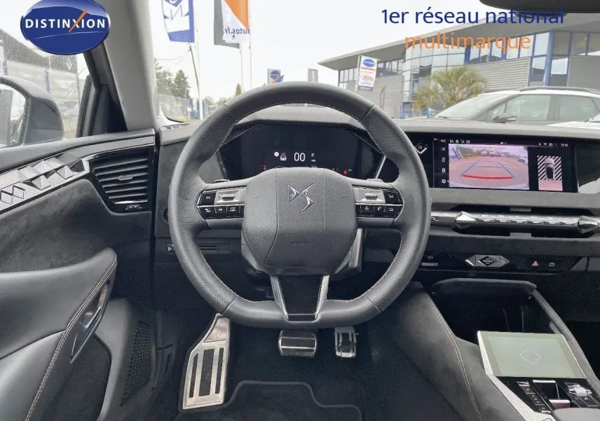 Vue intérieure centrée sur le volant cuir noir du DS4 2024, avec tableau de bord digital et écran multimédia affichant la caméra de recul.