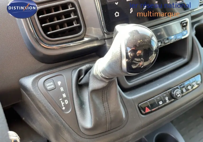 Gros plan sur le levier de vitesses automatique du Peugeot Boxer Fourgon blanc, avec tableau de bord et commandes visibles.