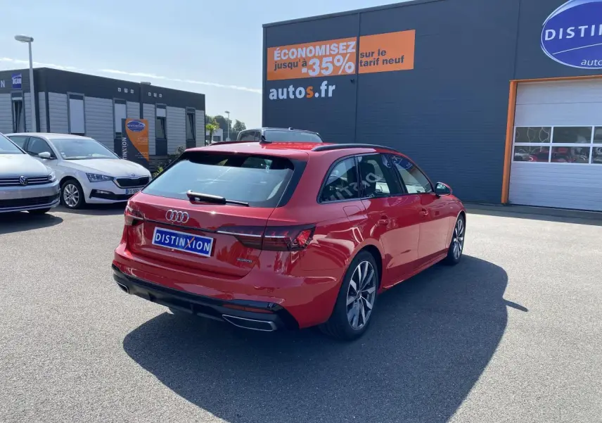 Audi A4 Avant S line rouge Tango vue 3/4 arrière droit sur parking devant un bâtiment commercial