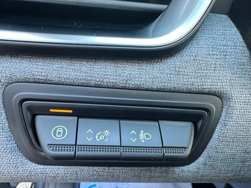 Gros plan sur les commandes de réglage des feux et verrouillage sur panneau textile gris à l'intérieur d'une Renault Clio Gris Rafale 2025