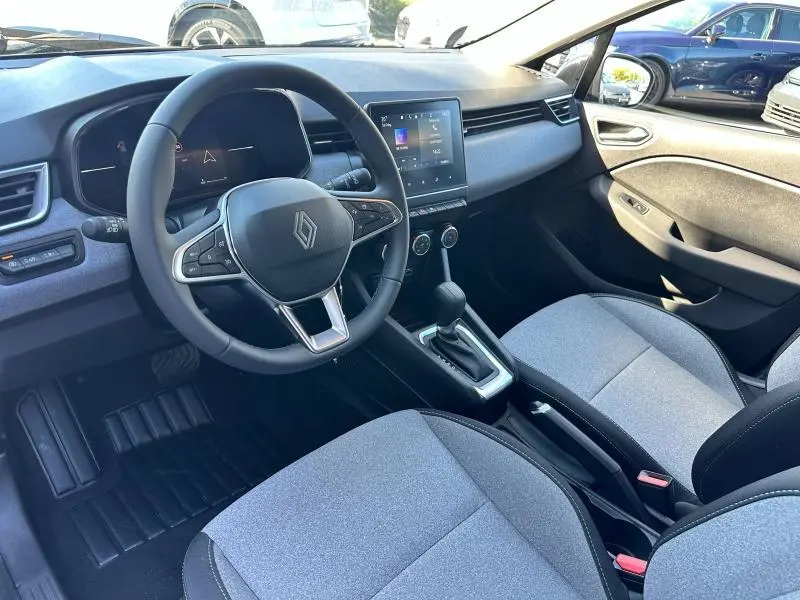 Intérieur de Renault Clio 2025 avec sièges gris, volant multifonction et écran tactile central visible côté conducteur.