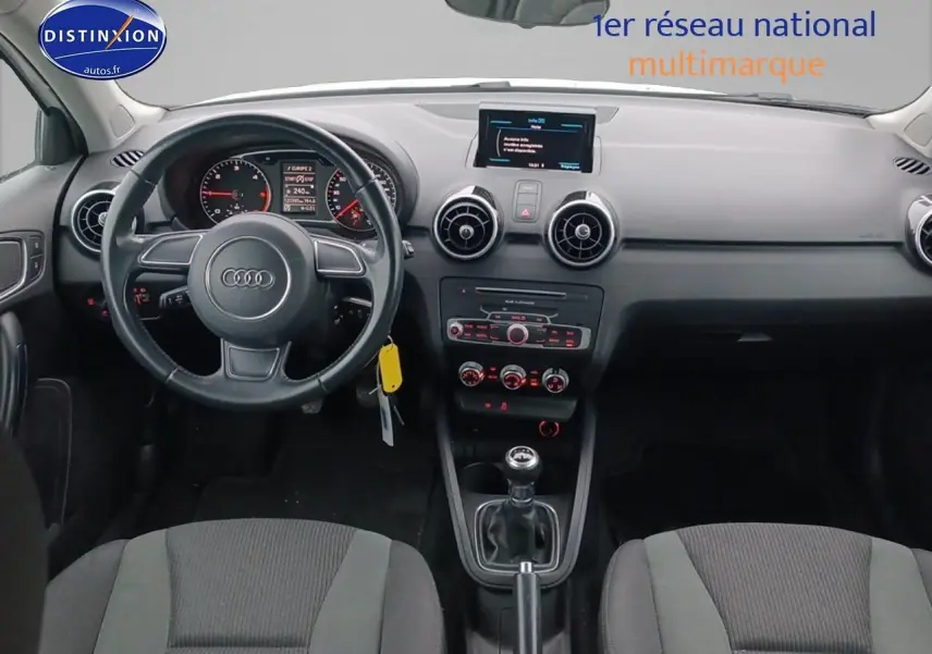 Vue intérieure frontale de l'Audi A1 blanche de 2015, avec tableau de bord noir et volant cuir multifonction.