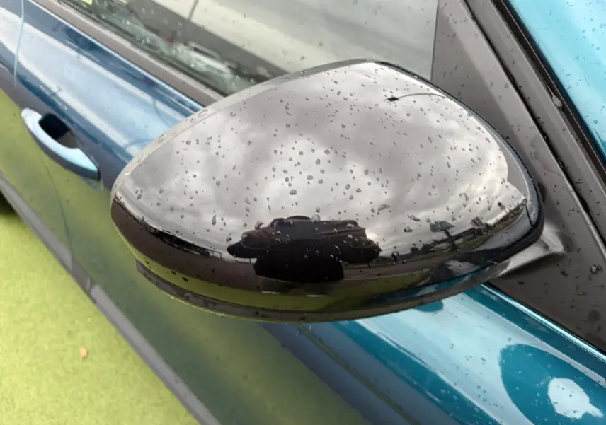 Rétroviseur droit noir brillant avec gouttes d'eau sur carrosserie Bleu Zanzibar d'une Renault Arkana 2025.