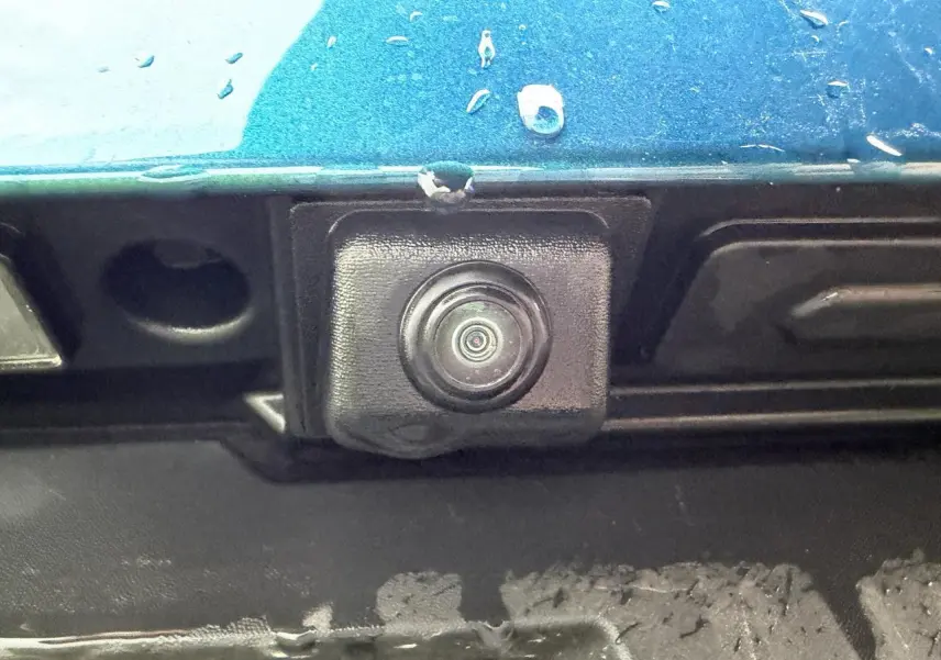 Gros plan sur la caméra de recul noire sous la malle arrière d’une Renault Arkana bleu Zanzibar métallisé.