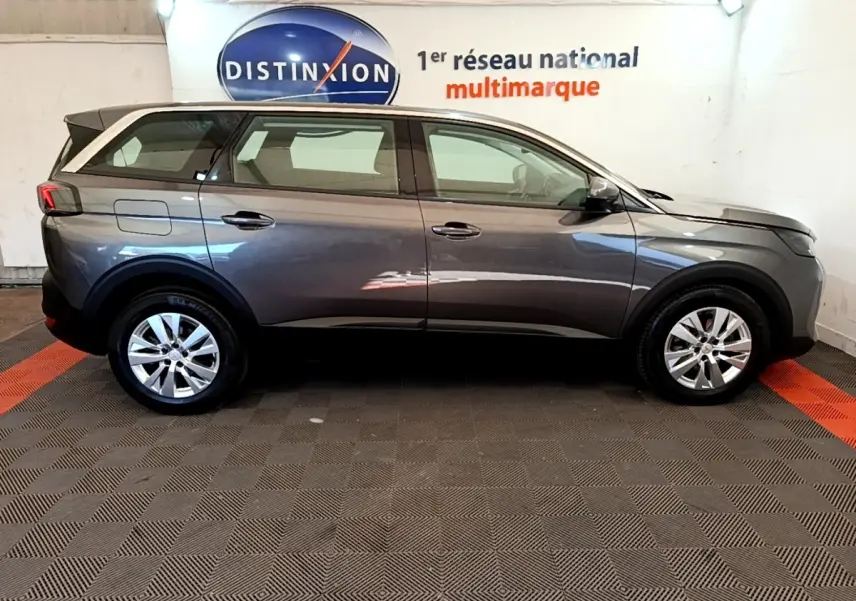 Profil droit d’un Peugeot 5008 gris clair 2021 garé en intérieur avec jantes alliage et rétroviseurs noirs.