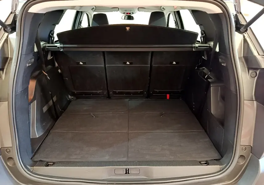 Coffre ouvert vu de l'arrière d'un Peugeot 5008 gris clair, banquette arrière rabattue et cache-bagages en place.