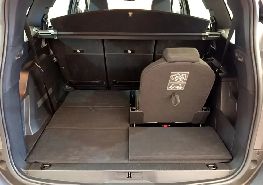 Vue arrière du coffre ouvert du Peugeot 5008 gris clair, montrant la troisième rangée de sièges partiellement rabattue.