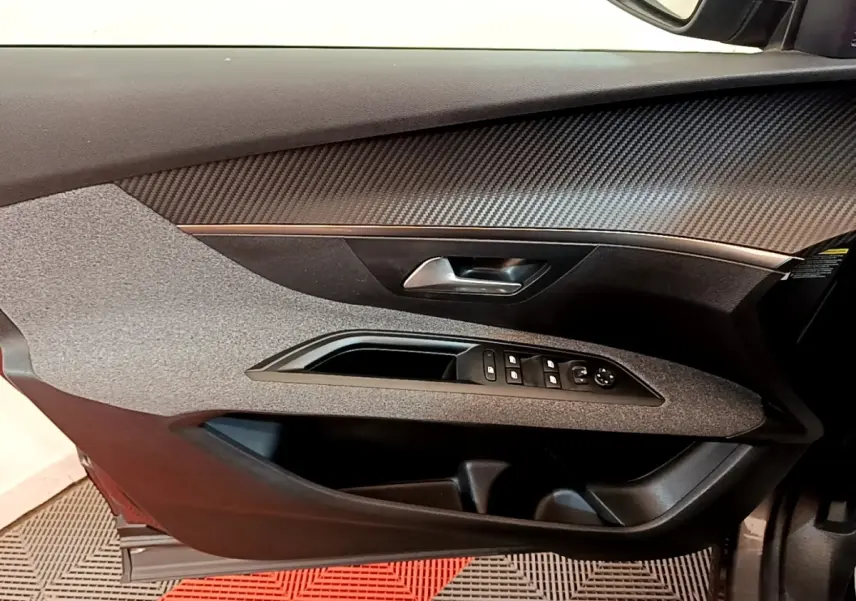 Vue intérieure du panneau de porte avant gauche du Peugeot 5008 gris clair, avec commandes électriques et poignée argentée.
