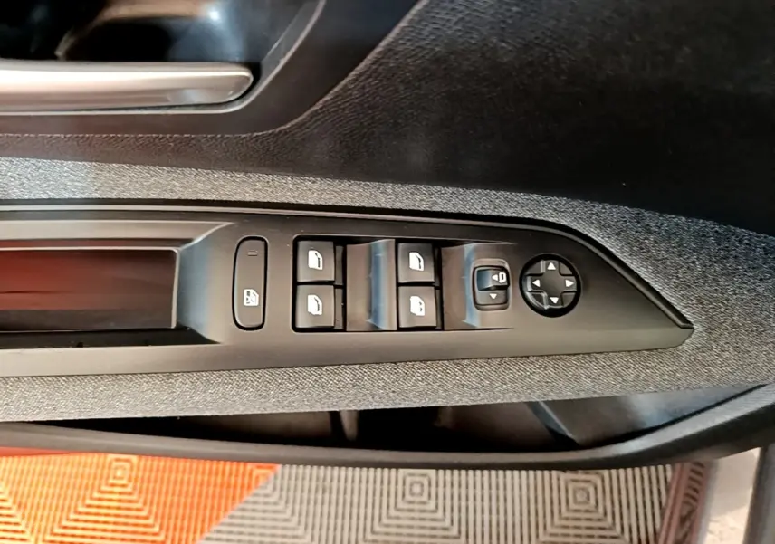 Détail des commandes des vitres électriques et rétroviseurs sur la porte côté conducteur d’un Peugeot 5008 gris clair.