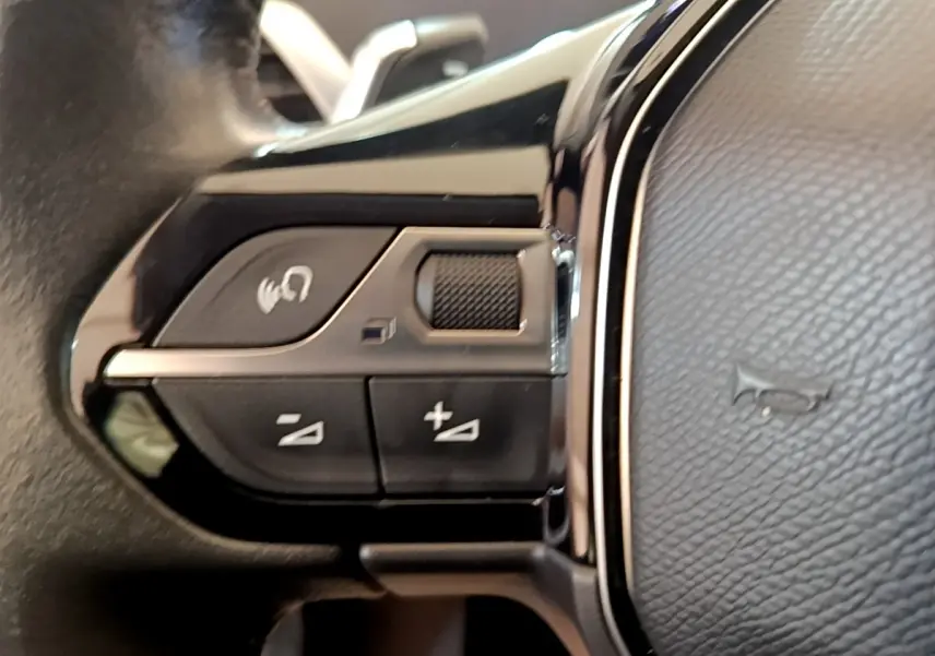 Gros plan sur les commandes de volume et appel vocal sur le volant cuir noir du Peugeot 5008 gris clair.