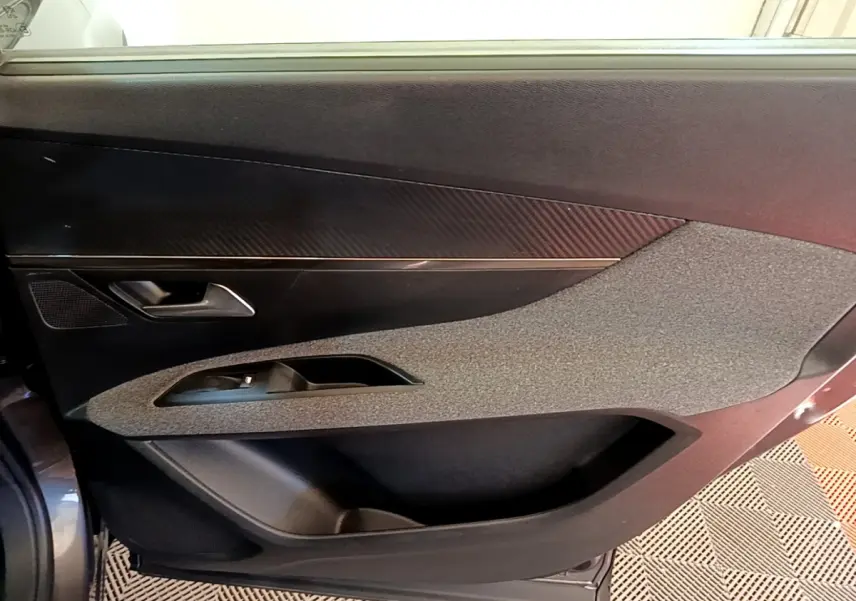 Vue intérieure côté gauche de la porte avant d’un Peugeot 5008 gris clair, avec habillage texturé et poignée argentée.