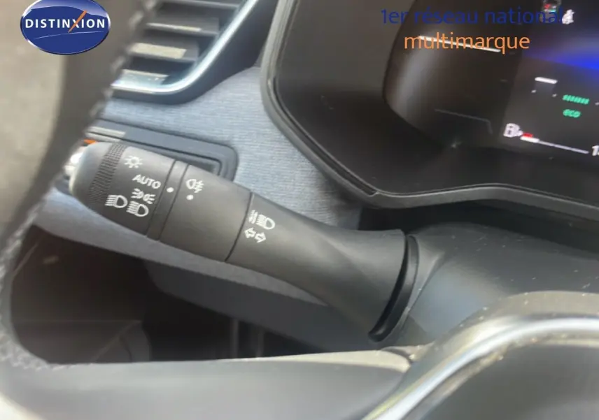 Gros plan sur la commande des feux et clignotants à gauche du volant dans l’habitacle d’une Renault Clio blanche.