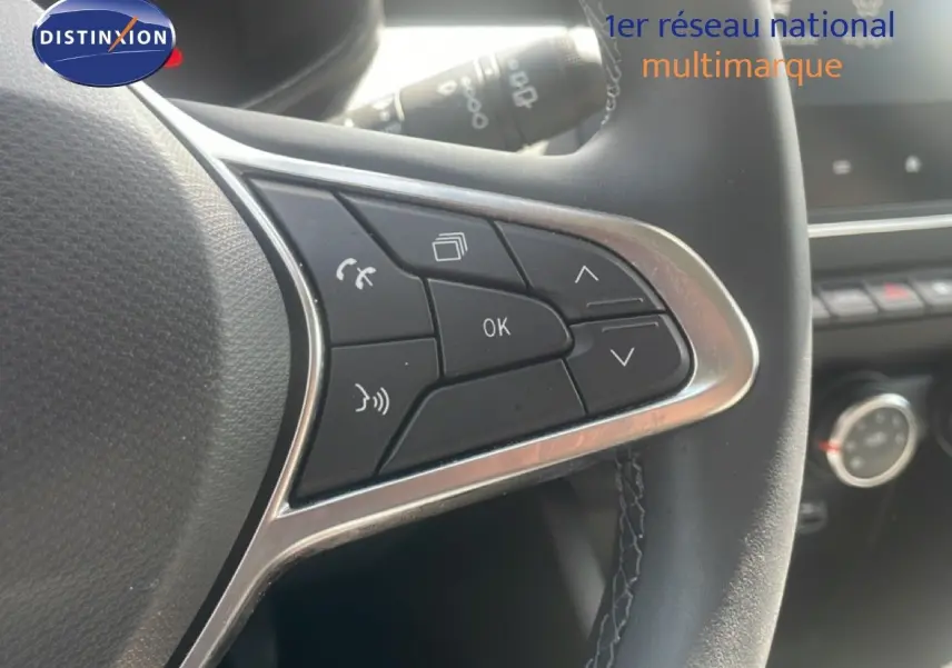 Gros plan sur les commandes multifonctions à droite du volant noir de la Renault Clio blanche, avec finition chromée.