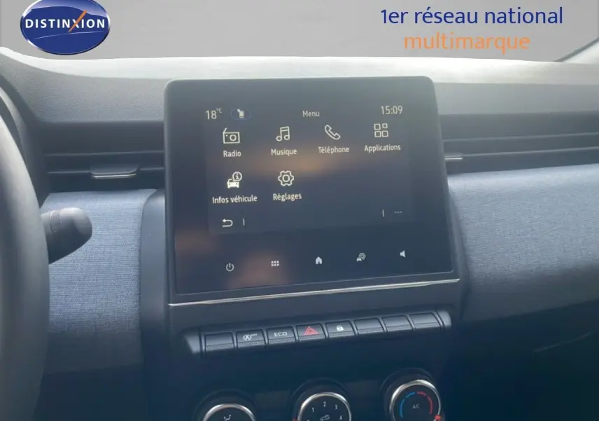 Vue intérieure centrée sur l’écran tactile du tableau de bord d’une Renault Clio blanche, avec commandes de climatisation visibles.