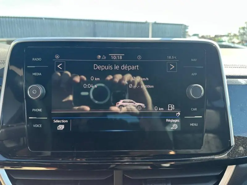 Écran tactile central du Volkswagen T-Roc 2025 affichant les données de trajet, avec reflet de mains et appareil photo.