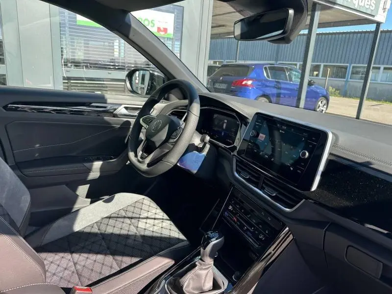 Vue intérieure côté conducteur du Volkswagen T-Roc noir nacré, mettant en valeur le volant cuir multifonction et l'écran tactile central.