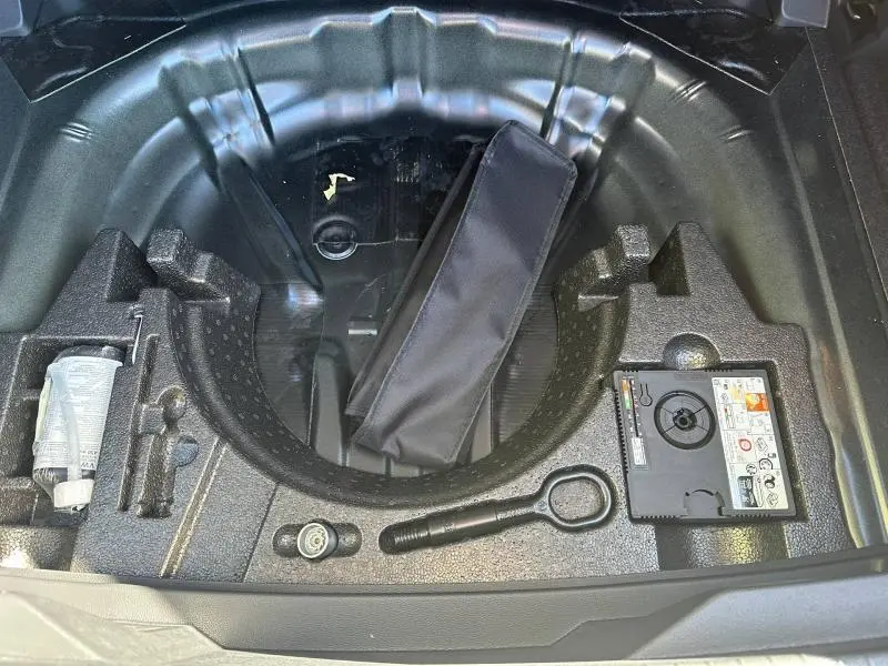 Vue plongeante sur le coffre ouvert d'un Volkswagen T-Roc 2025 noir, montrant le rangement sous la roue de secours.