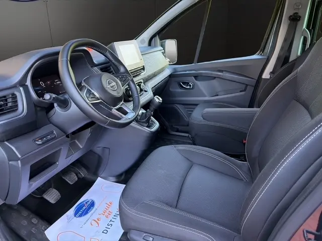 Vue intérieure côté conducteur du Nissan Primastar gris foncé 2025, avec tableau de bord moderne et volant multifonctions cuir.