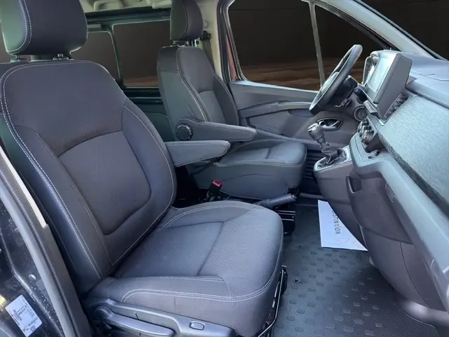 Vue intérieure côté conducteur du Nissan Primastar gris foncé 2025, montrant les sièges avant et le tableau de bord avec écran tactile.