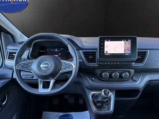 Vue intérieure avant du tableau de bord gris foncé du Nissan Primastar 2025 avec volant cuir et écran tactile central.