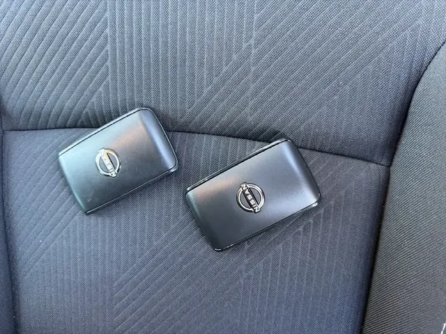 Gros plan sur deux clés noires Nissan posées sur un siège tissu gris foncé à motifs diagonaux.