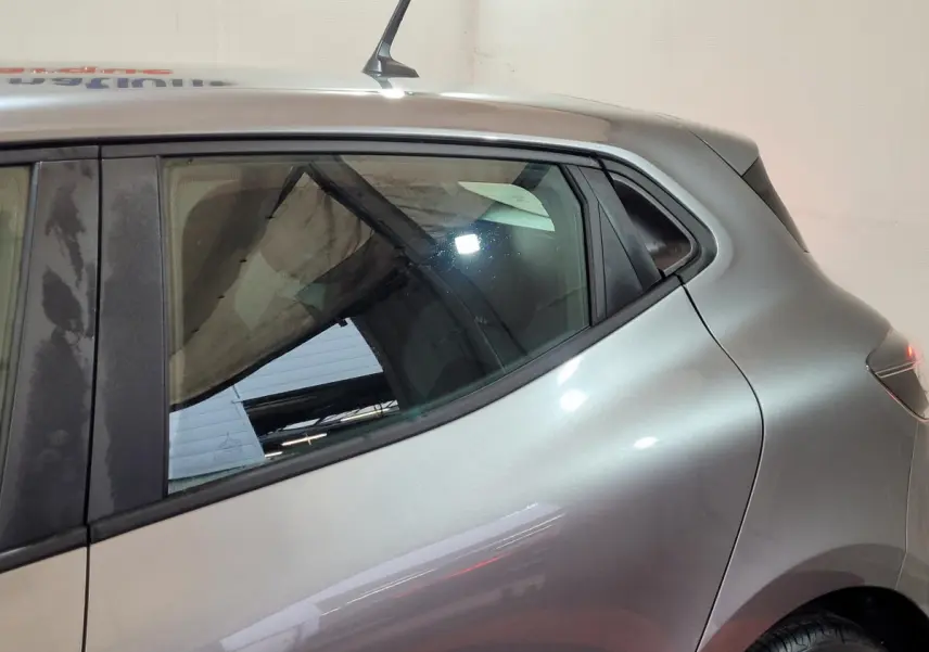 Vue latérale gauche rapprochée d’une Renault Clio gris foncé 2025, mettant en valeur la ligne de toit et la vitre arrière.