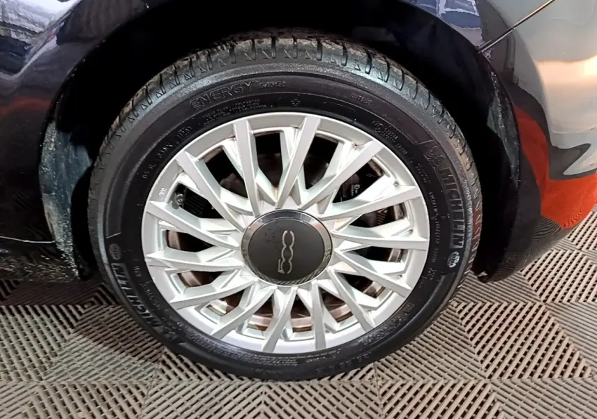 Gros plan sur la roue avant gauche d'une FIAT 500 noire, mettant en valeur la jante argentée au design fin et élégant.