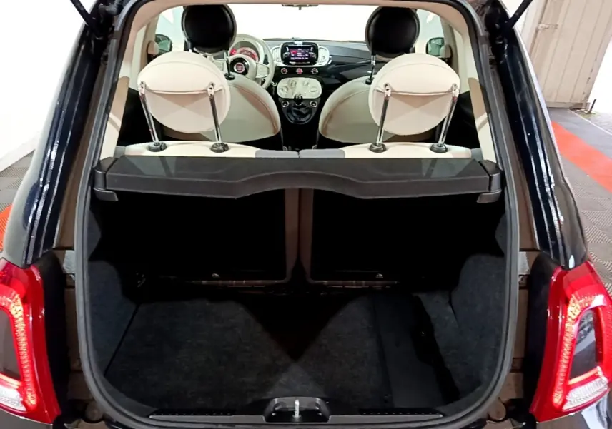 Coffre ouvert d’une Fiat 500 noire vue arrière, intérieur beige avec tableau de bord et écran tactile visibles.