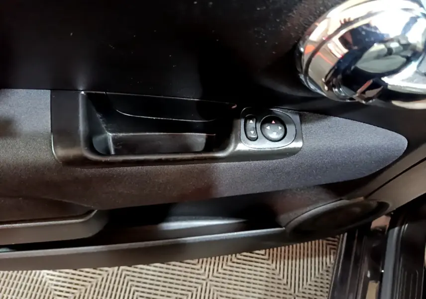 Gros plan sur la poignée intérieure et les commandes de réglage des rétroviseurs côté conducteur d'une Fiat 500 noire.