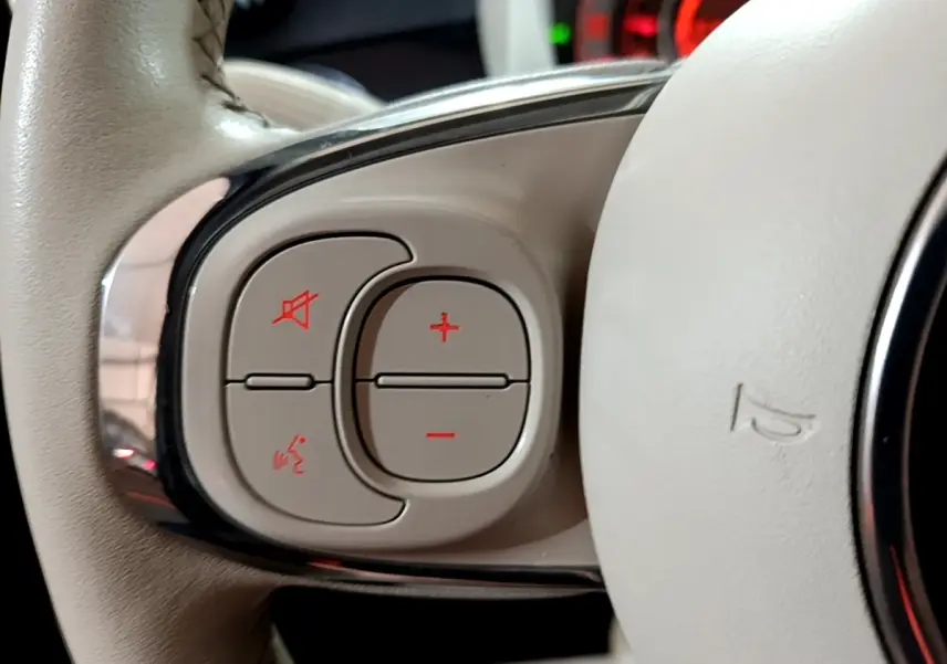 Gros plan sur les commandes du volant cuir beige de la Fiat 500 Lounge noire, avec boutons de volume et commande vocale.