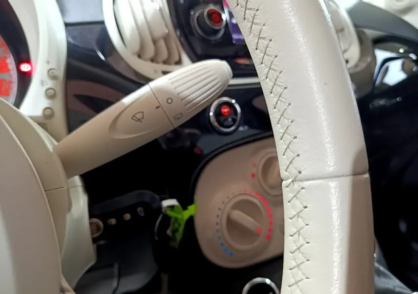 Gros plan sur le volant cuir beige et la commande d’essuie-glace de la Fiat 500 noire, tableau de bord en arrière-plan.