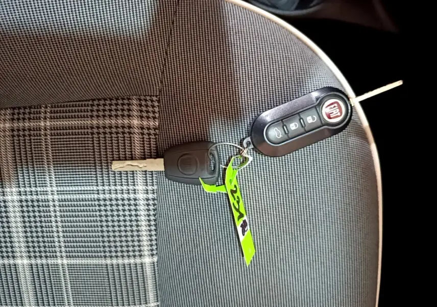 Clé et télécommande FIAT posées sur un siège tissu gris à motifs carreaux, intérieur d'une FIAT 500 noire.