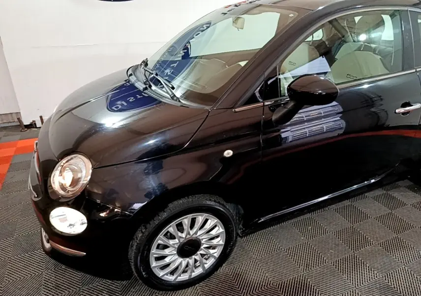 Vue 3/4 avant droit d'une FIAT 500 Lounge noire avec jantes alliage et intérieur clair visible.