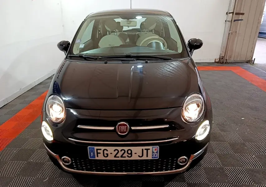 Vue avant d'une FIAT 500 noire de 2019 avec phares allumés dans un garage intérieur.
