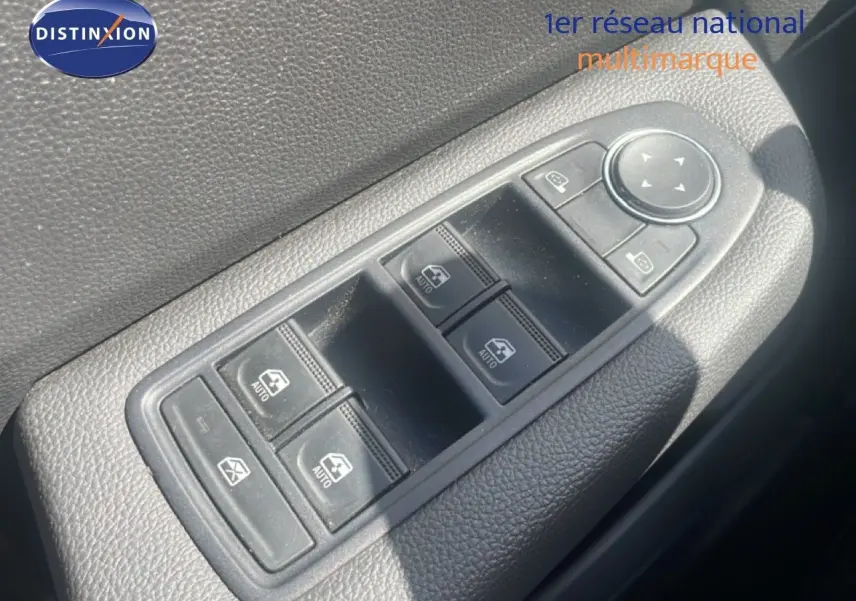 Gros plan sur les commandes des vitres électriques et rétroviseurs d'une Renault Clio blanche, côté intérieur porte avant.